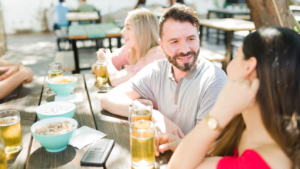 The image shows a man and woman, possibly on a date, enjoying a sunny day. The man's smile suggests he's engaged, reflecting the rule of showing genuine interest in conversation.