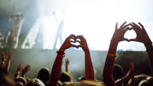 This photo captures a lively concert scene, with the audience showing their enthusiasm by forming heart shapes with their hands. It highlights how outdoor dates at events like music festivals can create a fun and energetic atmosphere, perfect for couples looking to share memorable experiences together.