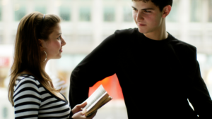 This image shows a young man and woman in a moment of conversation, with body language as the main focus. For those wondering, "How do you know if a girl is interested in you?", pay attention to signs like eye contact, open posture, and engagement in the conversation. These are subtle hints of interest.