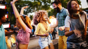 The purpose of the image is to capture the carefree, joyful energy of social gatherings. It raises the question, "Is she being friendly or flirty?" by highlighting the playful interactions and body language between the woman and the man, making it open to interpretation whether her behavior is casual or more intimate.