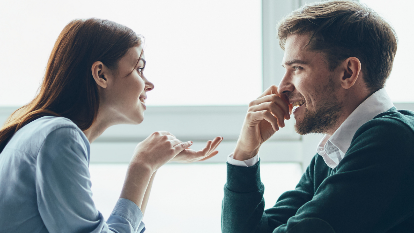 This image captures a lively moment between a young woman and a man, both engaged in a playful conversation. The woman's animated expression and hand gestures suggest she's sharing something exciting, while the man's amused smile indicates he’s fully captivated by her. This scene serves as a great example of what the signs of a girl flirting are.