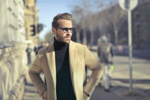 This image showcases a well-dressed man standing confidently on a city street, exuding sophistication and charm. The purpose of the image seems to be highlighting the impact of a polished look and confident demeanor. For those asking **how can I look attractive**, this suggests that combining stylish clothing, like a tailored camel coat and a sleek black turtleneck, with good posture and self-assurance can make a big difference.