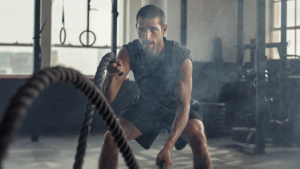 Man training with battle ropes in the gym, showing how to build confidence naturally through discipline, persistence, and self-improvement.
