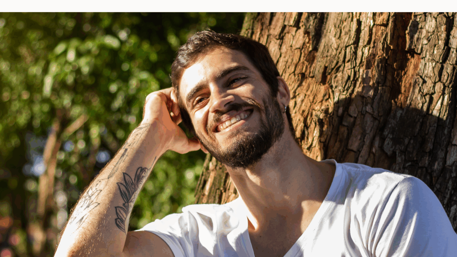 Smiling man sitting under a tree in sunlight, showing how to build confidence naturally by embracing self-acceptance and inner peace.