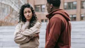 A couple sits facing away from each other with tense expressions, visually questioning the idea: do opposites attract in relationships or create conflict?