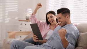 A happy couple celebrates while looking at a tablet, symbolizing emotional connection and shared joy.