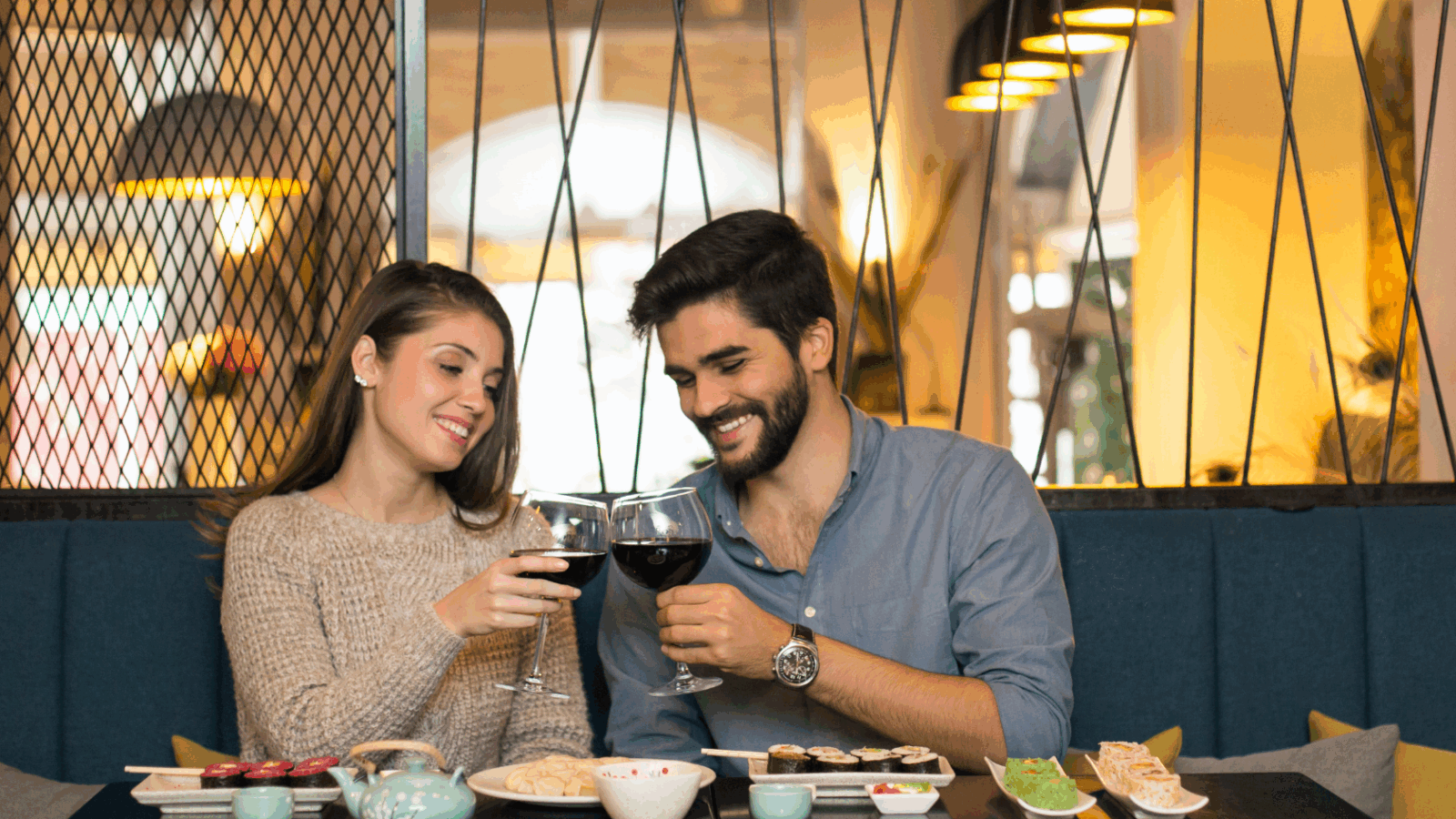 A couple smiling and clinking wine glasses over sushi during a cozy dinner date, capturing connection in dating as a quiet guy.