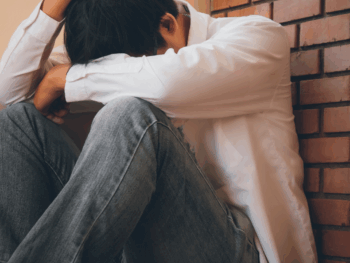 Man sitting against a wall holding his head, looking stressed and alone, symbolizing how to stop being desperate with women.