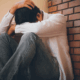 Man sitting against a wall holding his head, looking stressed and alone, symbolizing how to stop being desperate with women.