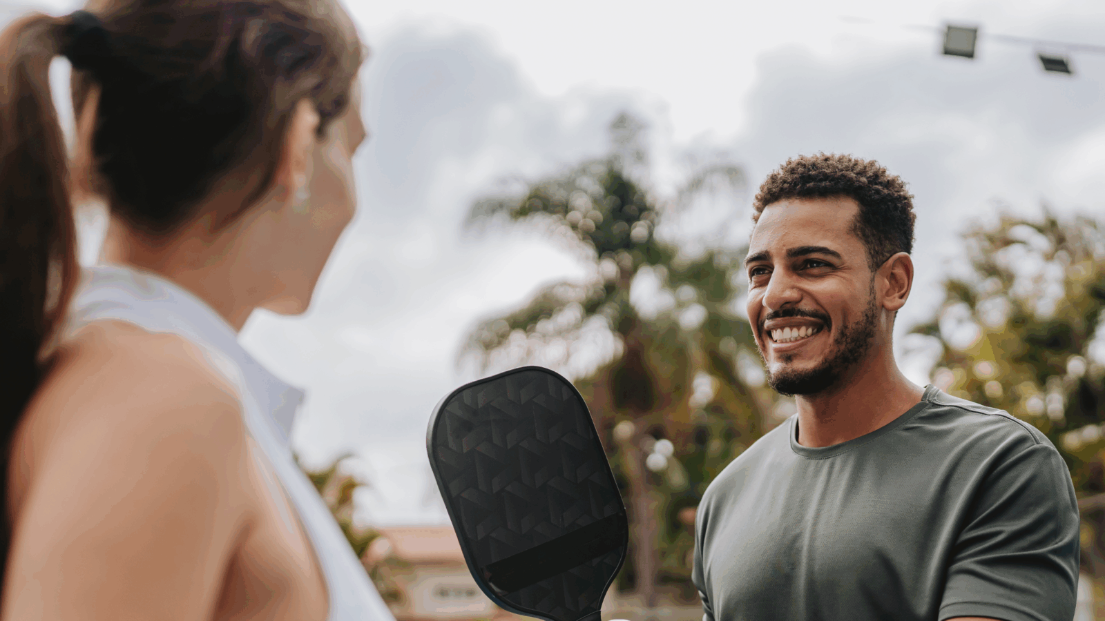 This image shows a natural, low-pressure conversation between a man and a woman during a pickleball game, illustrating how introverts talk to women by using the environment instead of direct compliments.