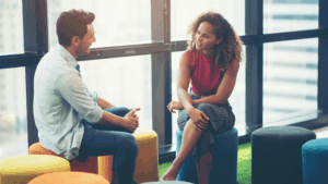 A man and woman sit across from each other in a bright lounge area, having a relaxed conversation &mdash; showing how-introverts-talk-to-women by focusing on calm, low-pressure one-on-one moments in natural settings, which is how introverts talk to women most comfortably.