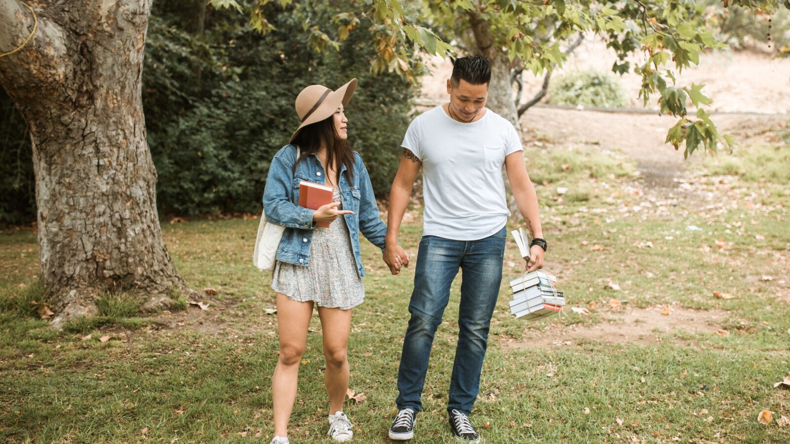 A young couple enjoying college dating, walking hand in hand on campus grounds while carrying their textbooks.