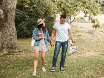 A young couple enjoying college dating, walking hand in hand on campus grounds while carrying their textbooks.