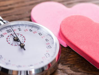 Silver stopwatch beside two paper hearts on a wooden table, illustrating the timed five-minute rounds of speed dating.