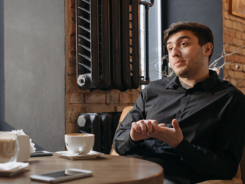 AI dating advice — man talking at coffee shop table with phone and coffee nearby