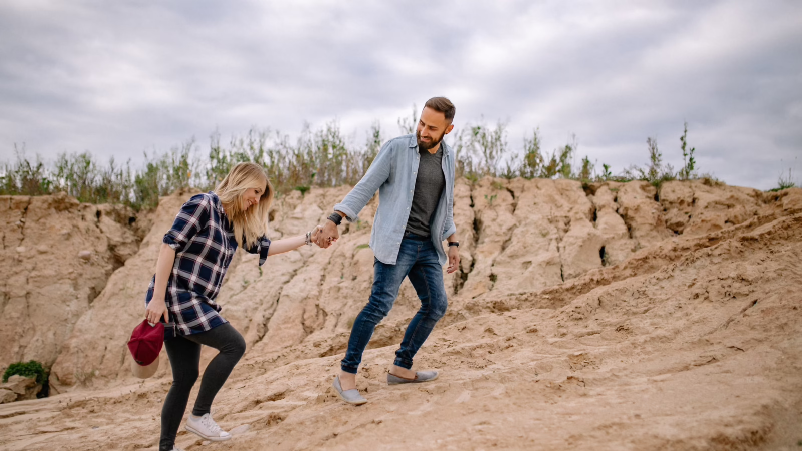 Couple holding hands while hiking down a sandy hill, one of the thrilling date ideas beyond dinner and a movie